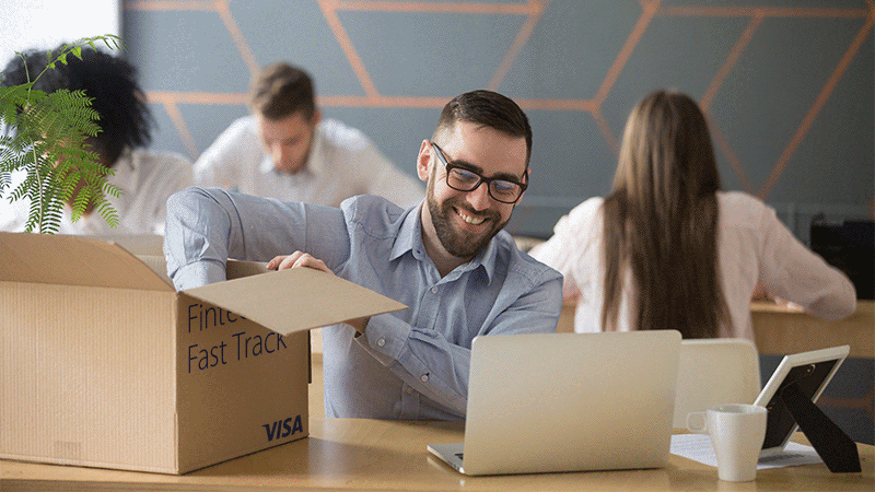 smiling man in office looking at laptop on desk and unpacking box